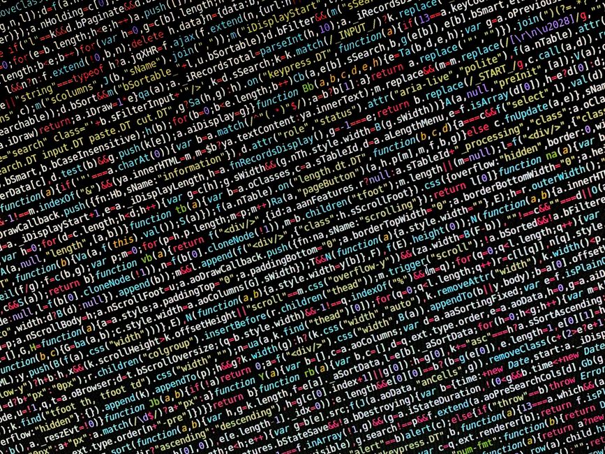 A person is seated at a desk inside a property, engaged in packing or setting up equipment for home relocation. They are facing a laptop that displays a screen filled with colorful lines of code or da