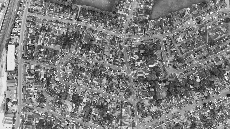 Aerial black-and-white photograph of a densely built residential area featuring numerous small houses and terraced rows, with narrow, winding streets and alleyways connecting properties. The rooftops 